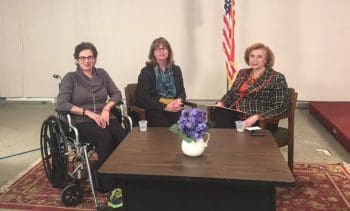 Three women seated, one in a wheelchair, around a coffee table.