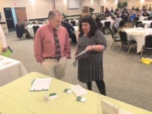 A man and woman talking at a vendor table in a conference space.