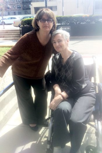Two women, one standing and one seated in a manual wheelchair