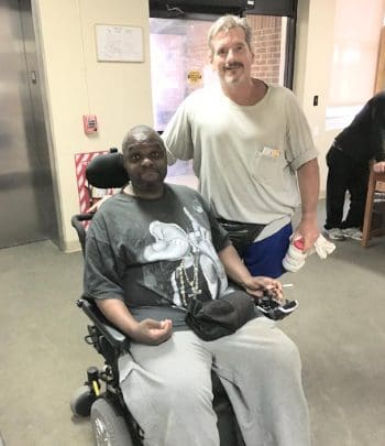 Two men, one seated in a power wheelchair