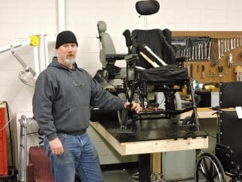 A man stands next to a workbench with a wheelchair and tools