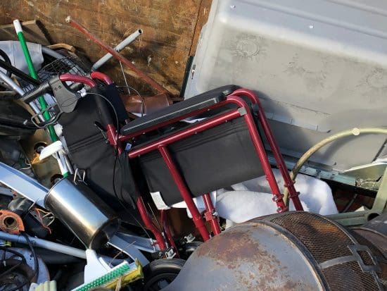 A folded transport wheelchair in a heap of garbage