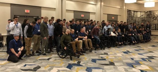 Two rows of employees smiling for a picture, the front row seated in manual wheelchairs. 