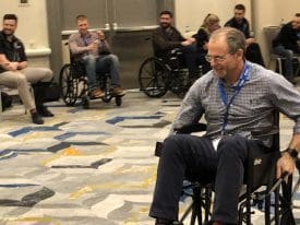 Men operating manual wheelchairs in a conference hall. 