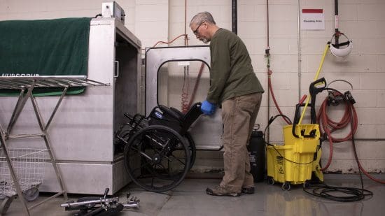 A man loading a wheelchair into a hubscrub cleaning machine.