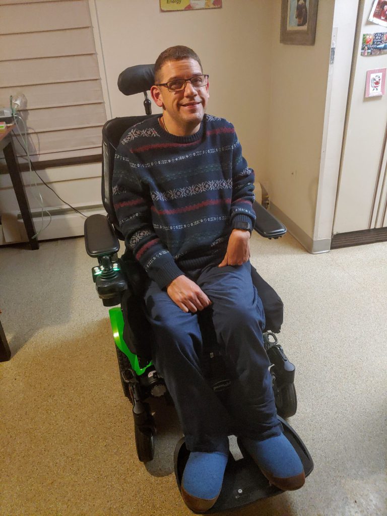 A man smiles seated in his power wheelchair.