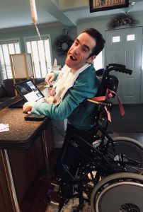 A smiling man using a standing wheelchair at a kitchen counter with an iPad.