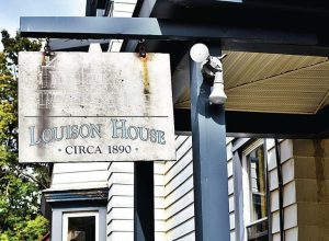 A sign mounted to hang off a clapboard house reads Louison House circa 1890.