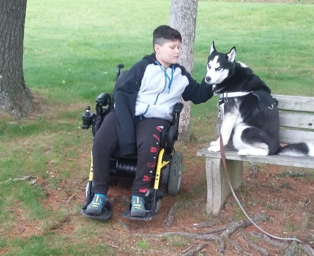 Boy in motorized wheelchairs with dog sitting on a bench