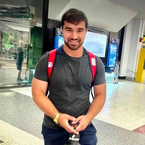 A fit young man stands smiling.