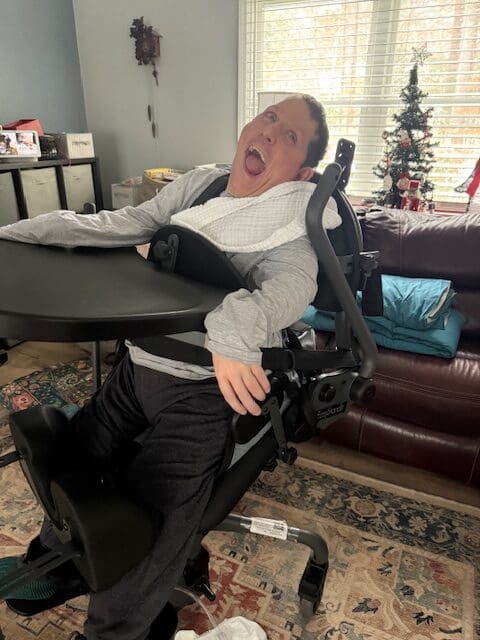 A man using a stander with holiday decorations behind him smiles broadly.