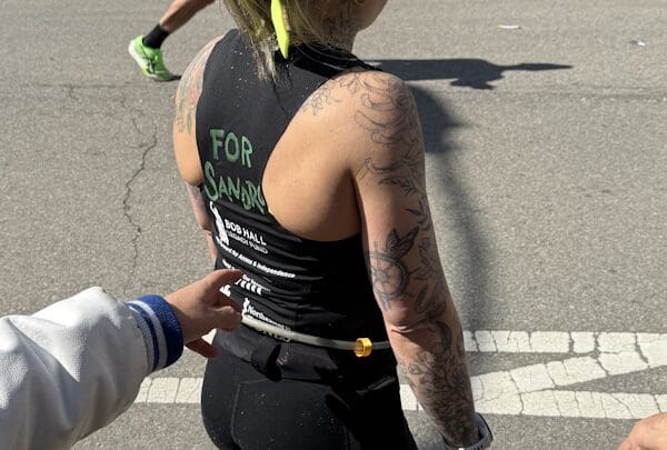 A hand points to the back of a runner's shirt that reads "For Sandro"
