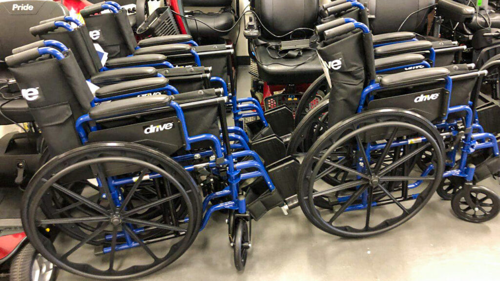 Several blue manual wheelchairs arranged among power wheelchairs in a medical equipment storage area.