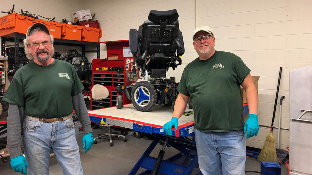 Two REquipment staff members beside a power wheelchair in the Worcester refurbishment workshop.
